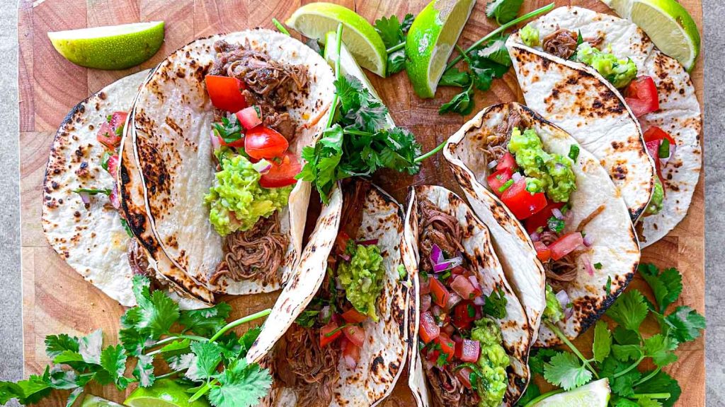 A chopping board filled with crockpot lamb barbacoa tacos.
