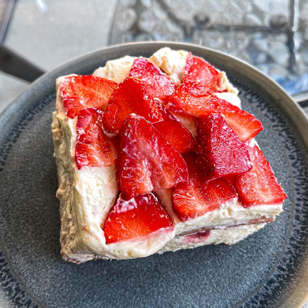 A slice of strawberry tiramisu, served on a dark plate.