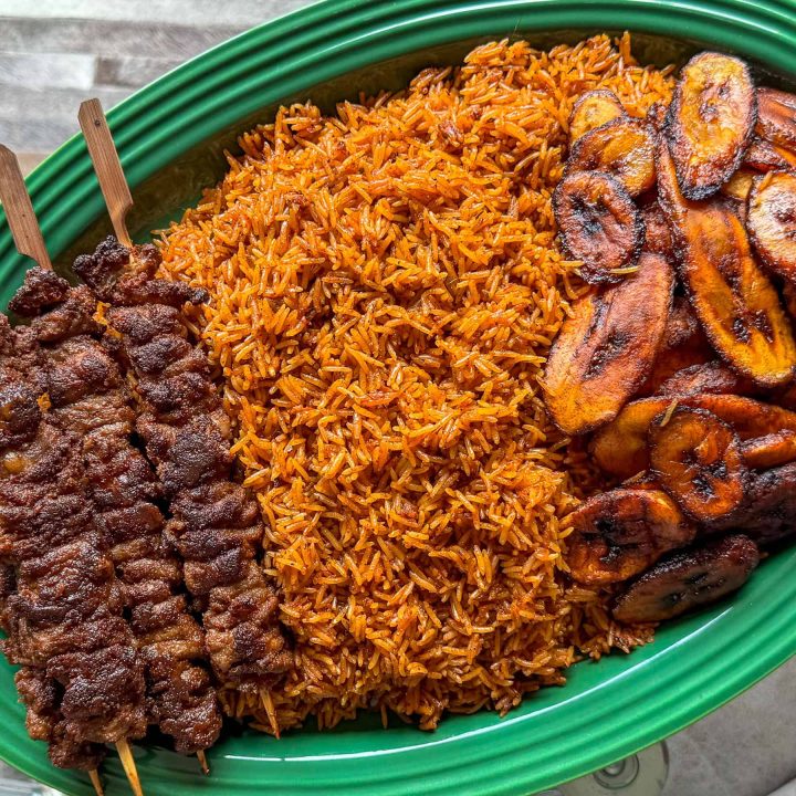 Nigerian jollof rice, served on a green platter with beef soya and fried plantain