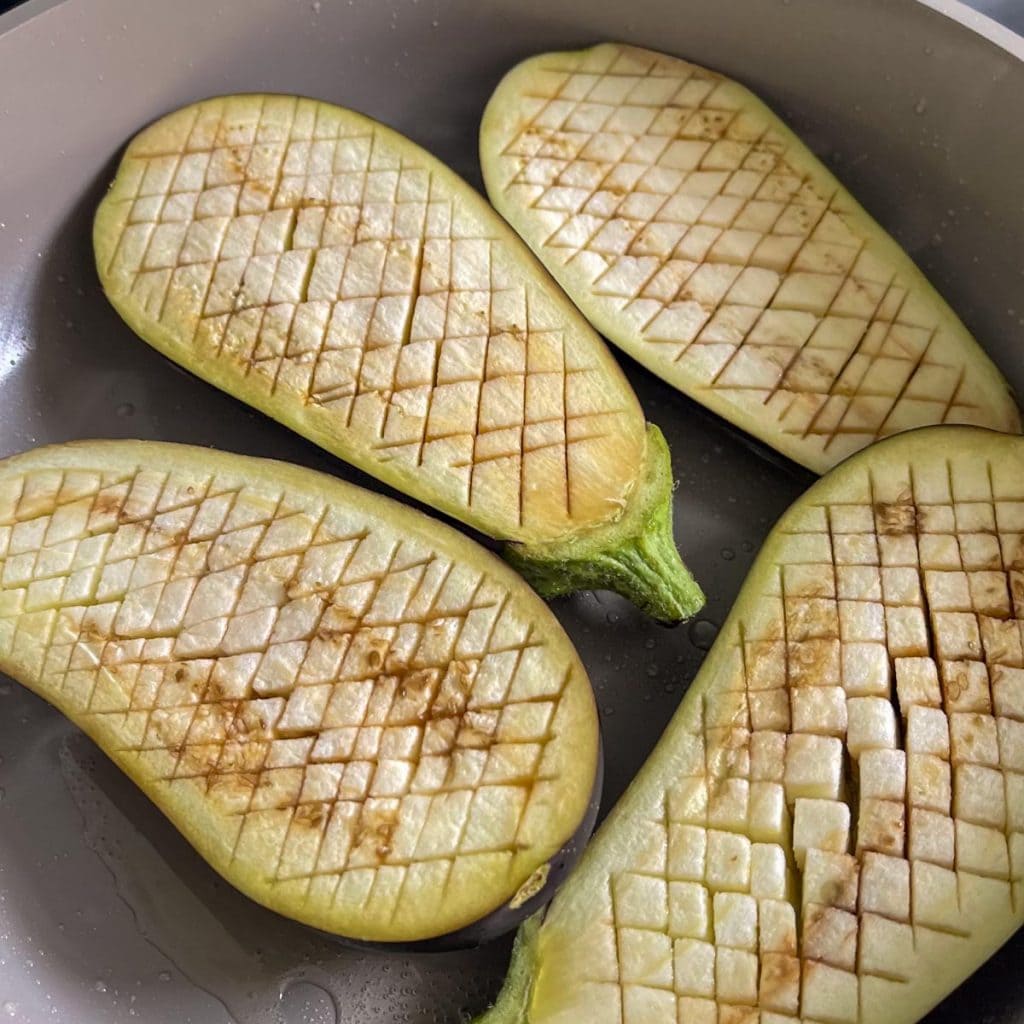 Scored aubergines frying skin-side-down in the pan
