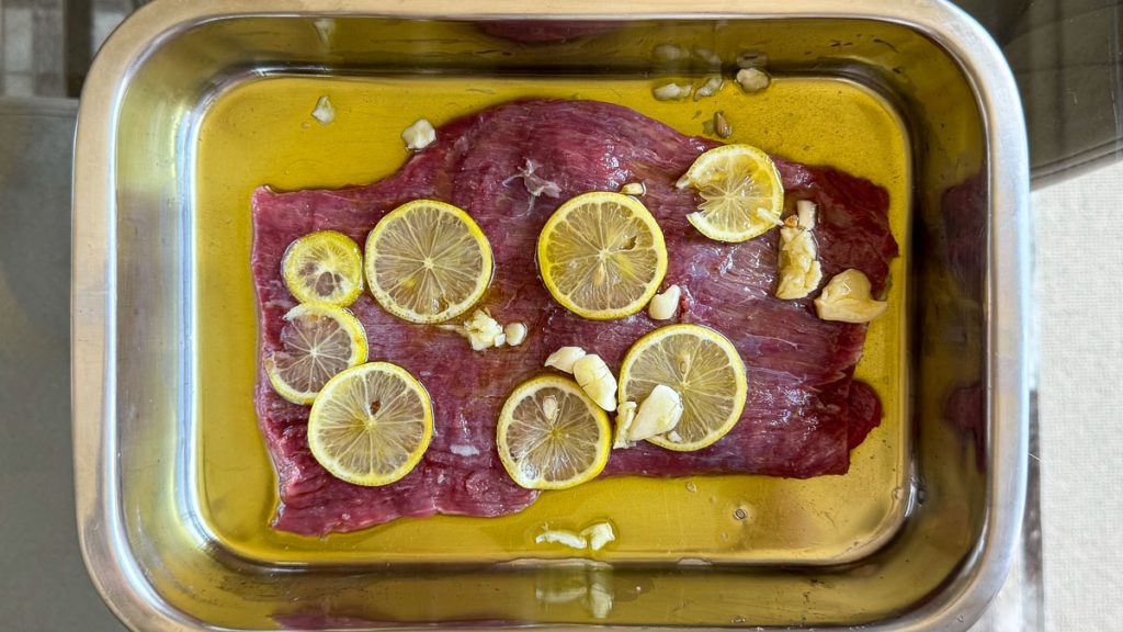 Marinating a flank steak in olive oil, garlic and lemon slices.