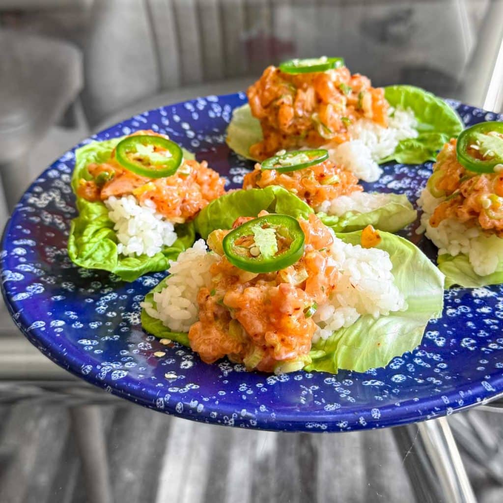 Side angle shot of Spicy Salmon Lettuce Cups arranged on a plate, ready to serve with fresh lime wedges.