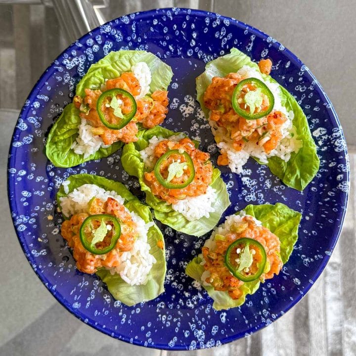 Overhead view of Spicy Salmon Lettuce Cups on a blue serving platter, garnished with jalapeño slices.