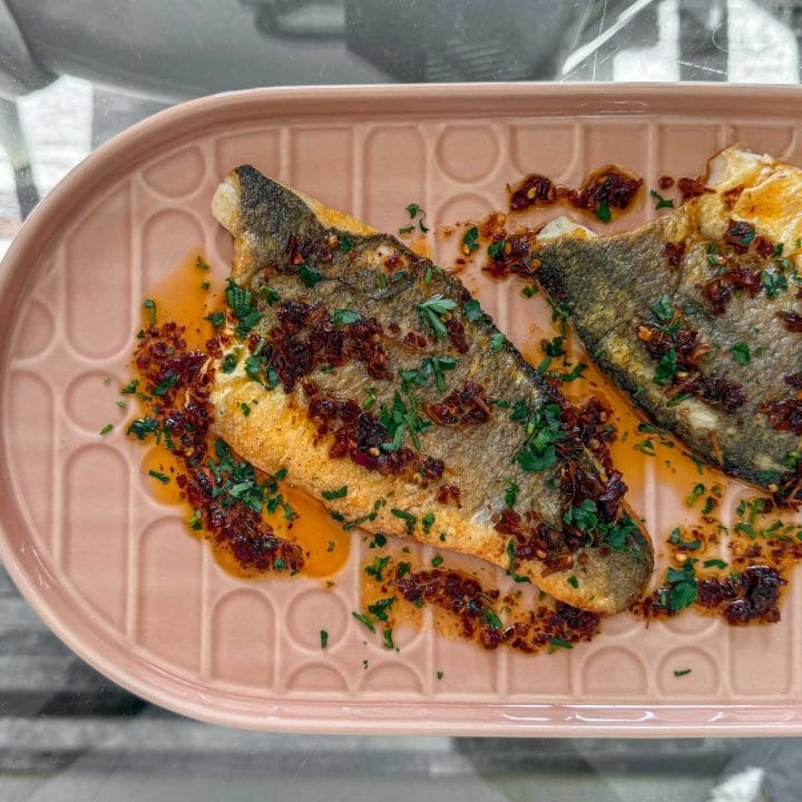 Close-up of golden-skinned sea bass with a spoonful of vibrant red chilli and lemongrass sauce glistening on top.
