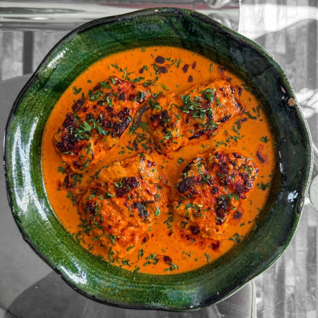 Plated cod in a rich sambal and coconut sauce on a green plate, photographed overhead to show char.