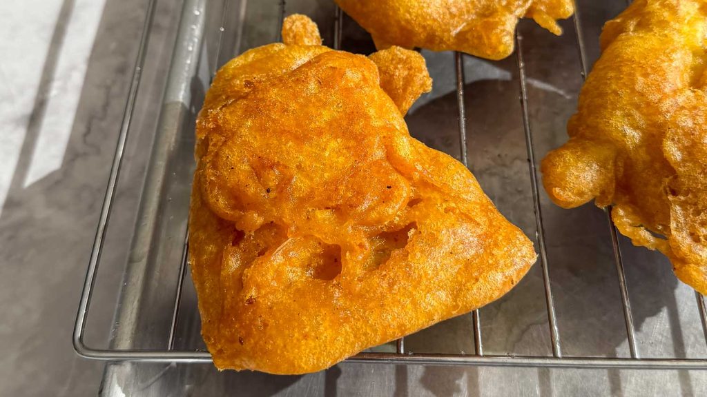 Close-up of battered cod draining on a rack, crust glistening and textured from the spiced beer batter.