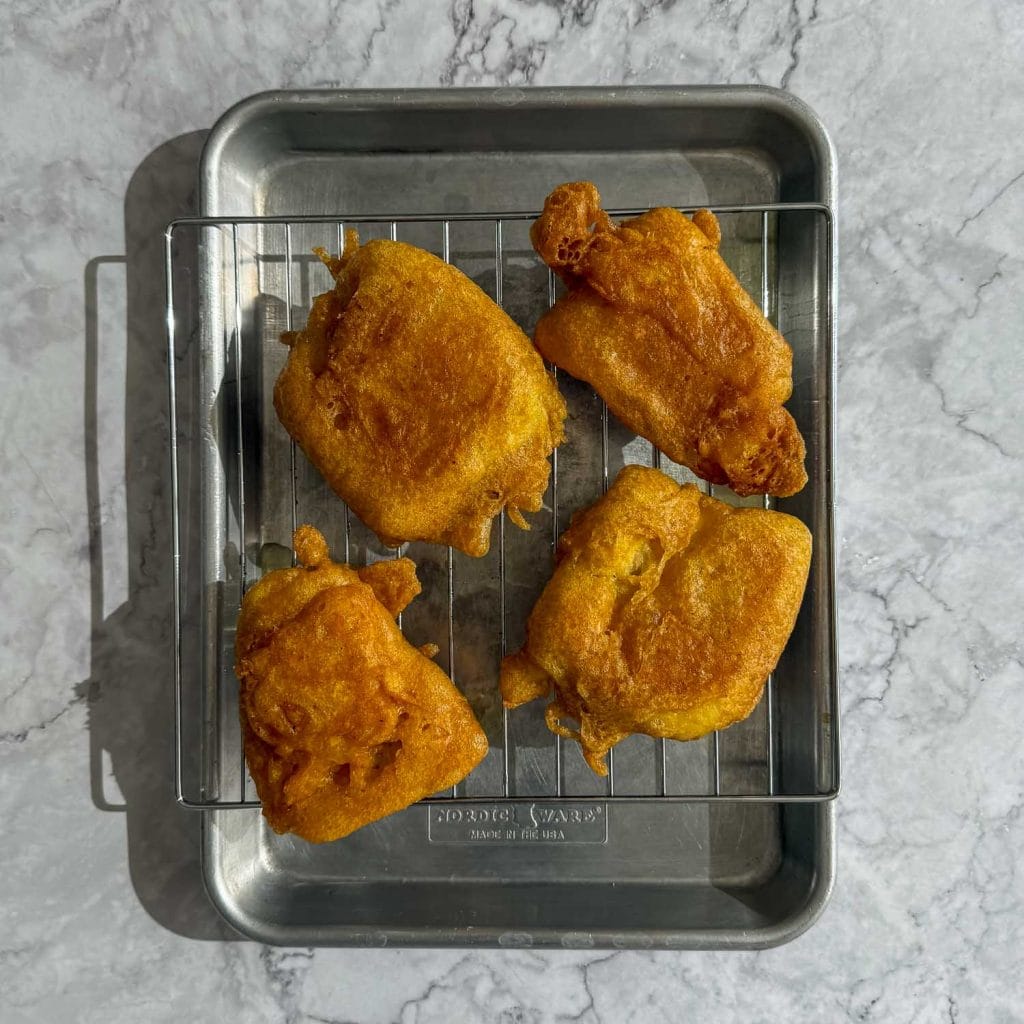 Freshly fried curried fish fillets resting on a wire rack, golden and crisp after coming out of the oil.
