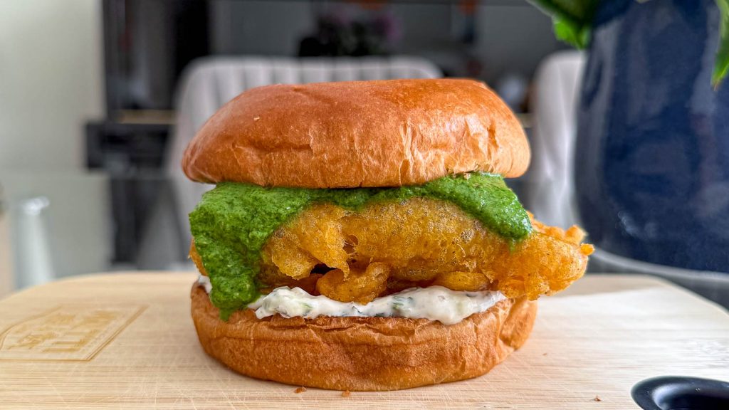 Crispy spiced cod in a toasted brioche bun layered with cooling raita and vibrant green chutney.