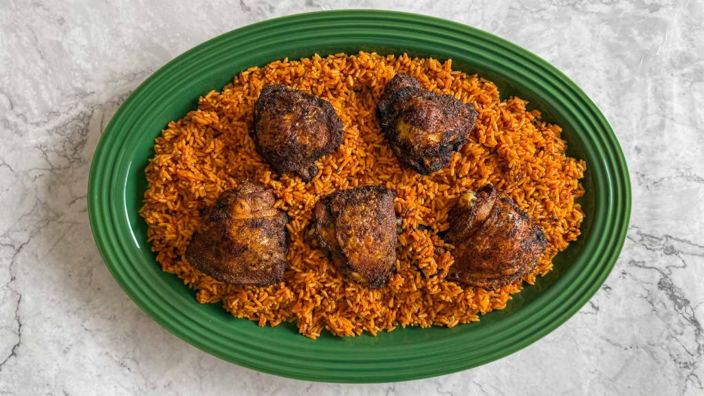 Oven grilled chicken, served over jollof rice, on a green platter.