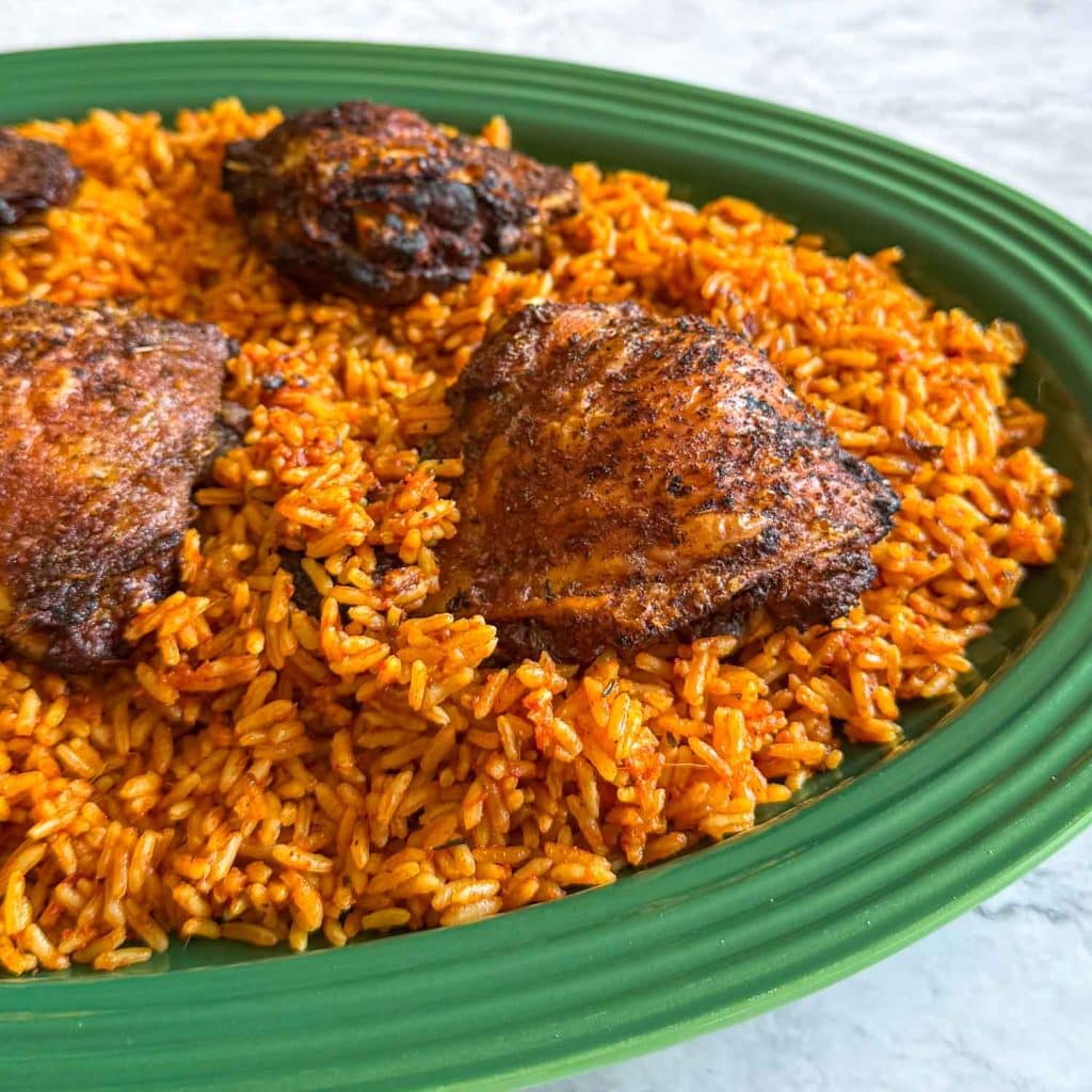 A close up of grilled chicken, served over Jollof Rice, on a green platter.