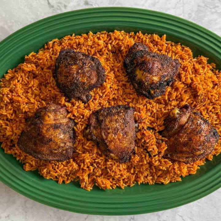Grilled chicken, served over Jollof Rice, on a green platter.