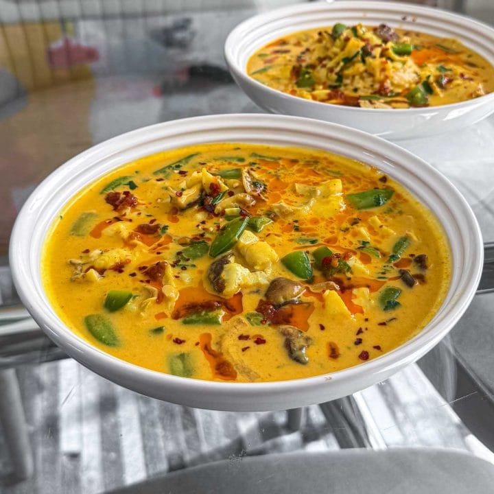 A close up of the Thai curry fish soup, served in a white shallow bowl.