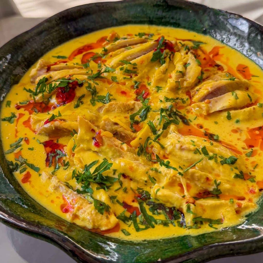 Close-up of Coconut Saffron Poached Chicken in a silky yellow saffron broth.