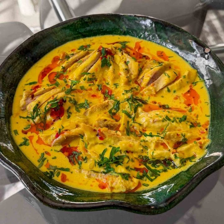 Coconut Saffron Poached Chicken served in a green shallow bowl with a golden saffron coconut broth.
