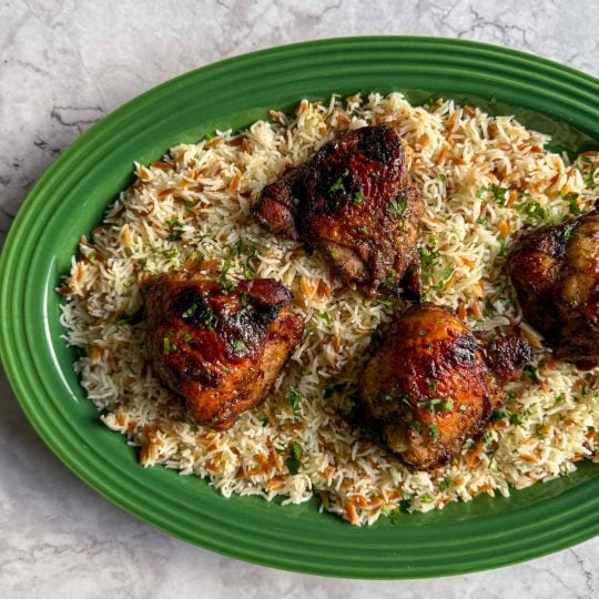 Sticky sumac chicken, served over Lebanese-style rice one a green platter.