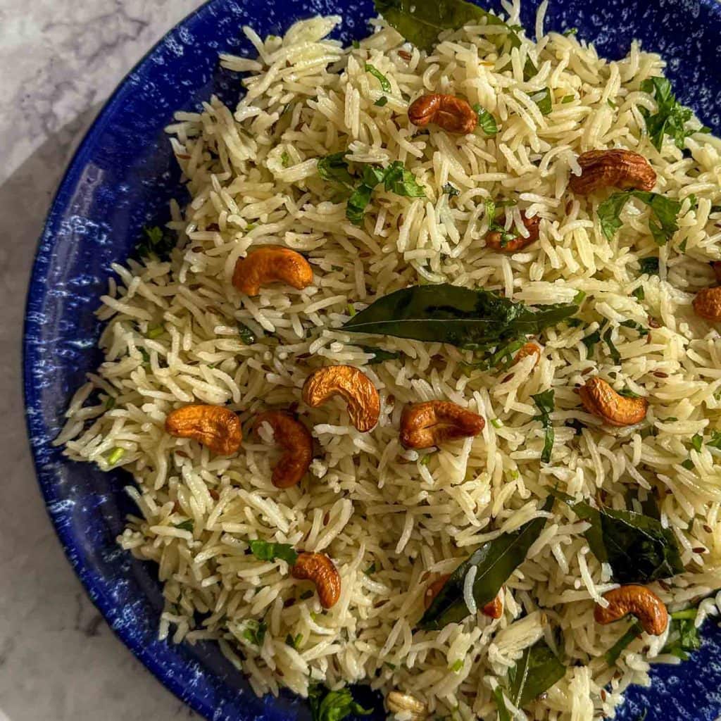 A close up of Spiced Curry Leaf Rice served on a blue plate, showing fluffy basmati rice with curry leaves.