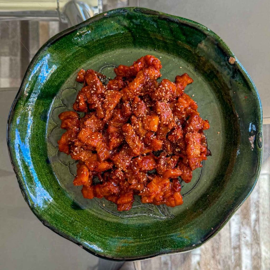 An overhead shot of sticky kimchi pork belly, served on a green plate.