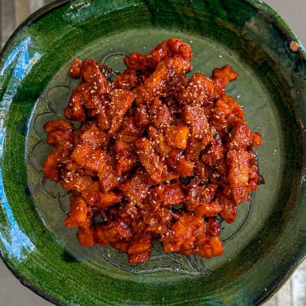 Sticky kimchi pork belly, served on a green plate, stopped with sesame seeds.