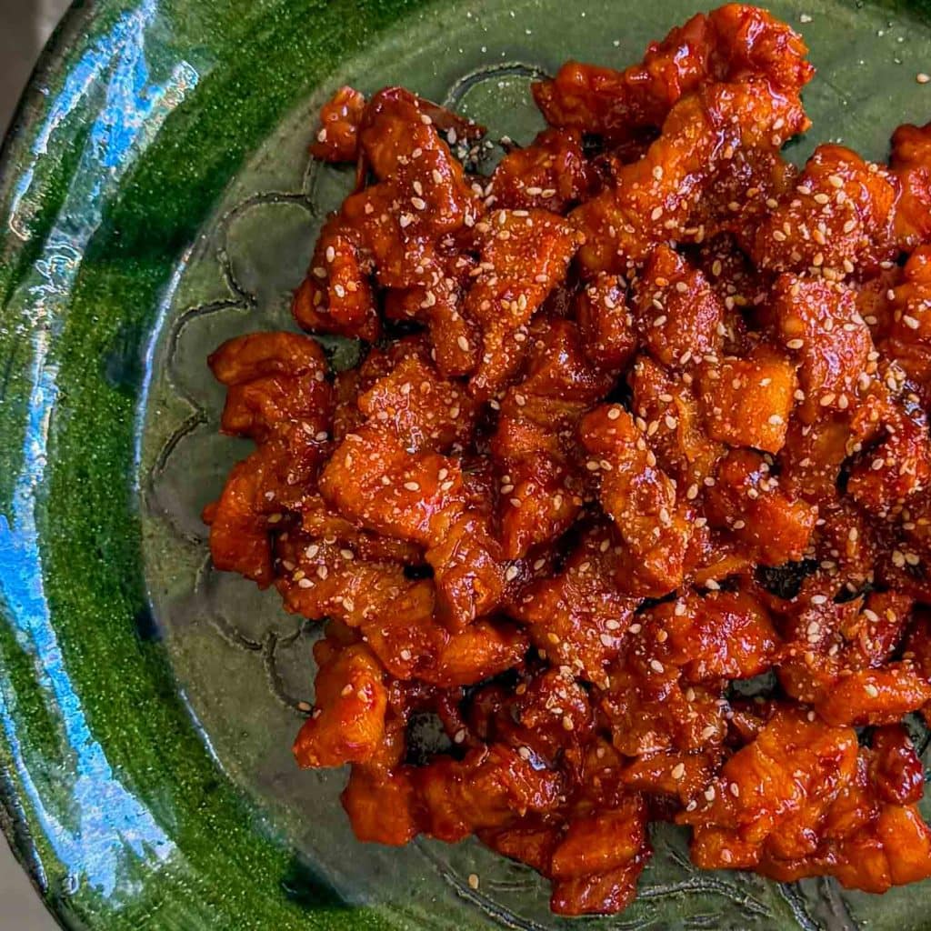 Sticky kimchi pork belly, served on a green plate.