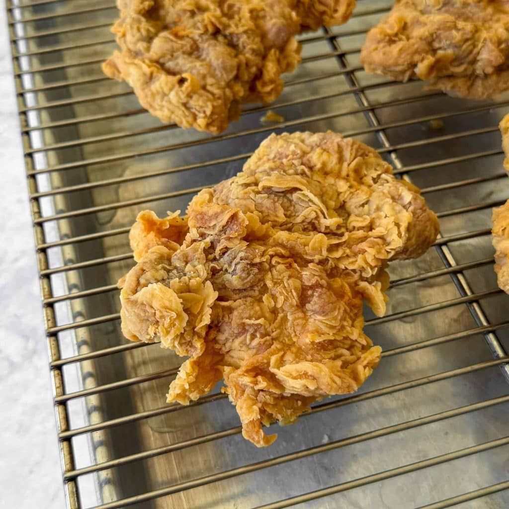 A side-on shot of ayam geprek, aka Indonesian smashed fried chicken, resting on a wire rack.