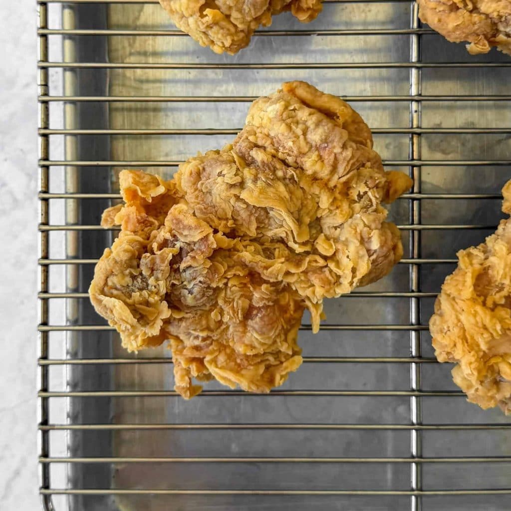 A close up of ayam geprek, aka Indonesian smashed fried chicken, resting on a wire rack.