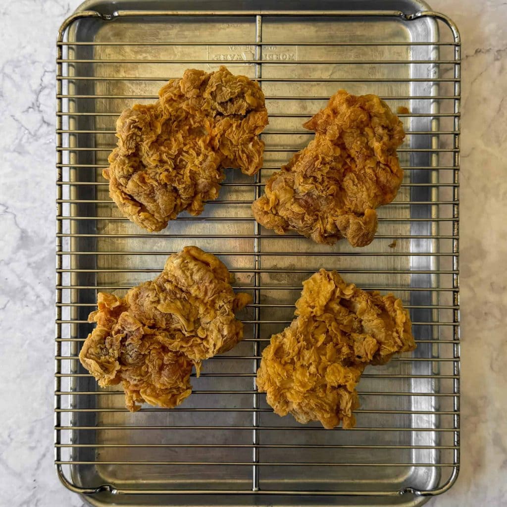 Ayam geprek, aka Indonesian smashed fried chicken, resting on a wire rack.
