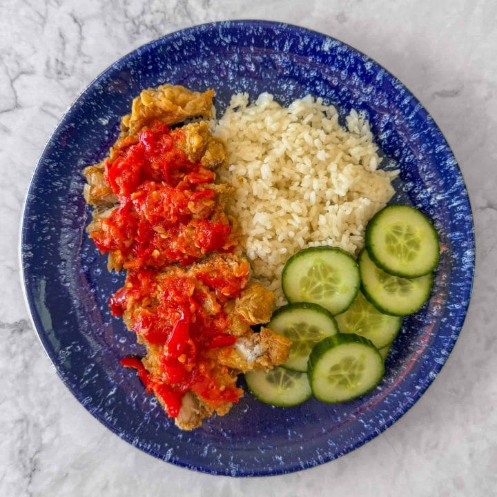 Ayam geprek, aka Indonesian smashed fried chicken, topped with sambal and served with rice and cucumber slices.