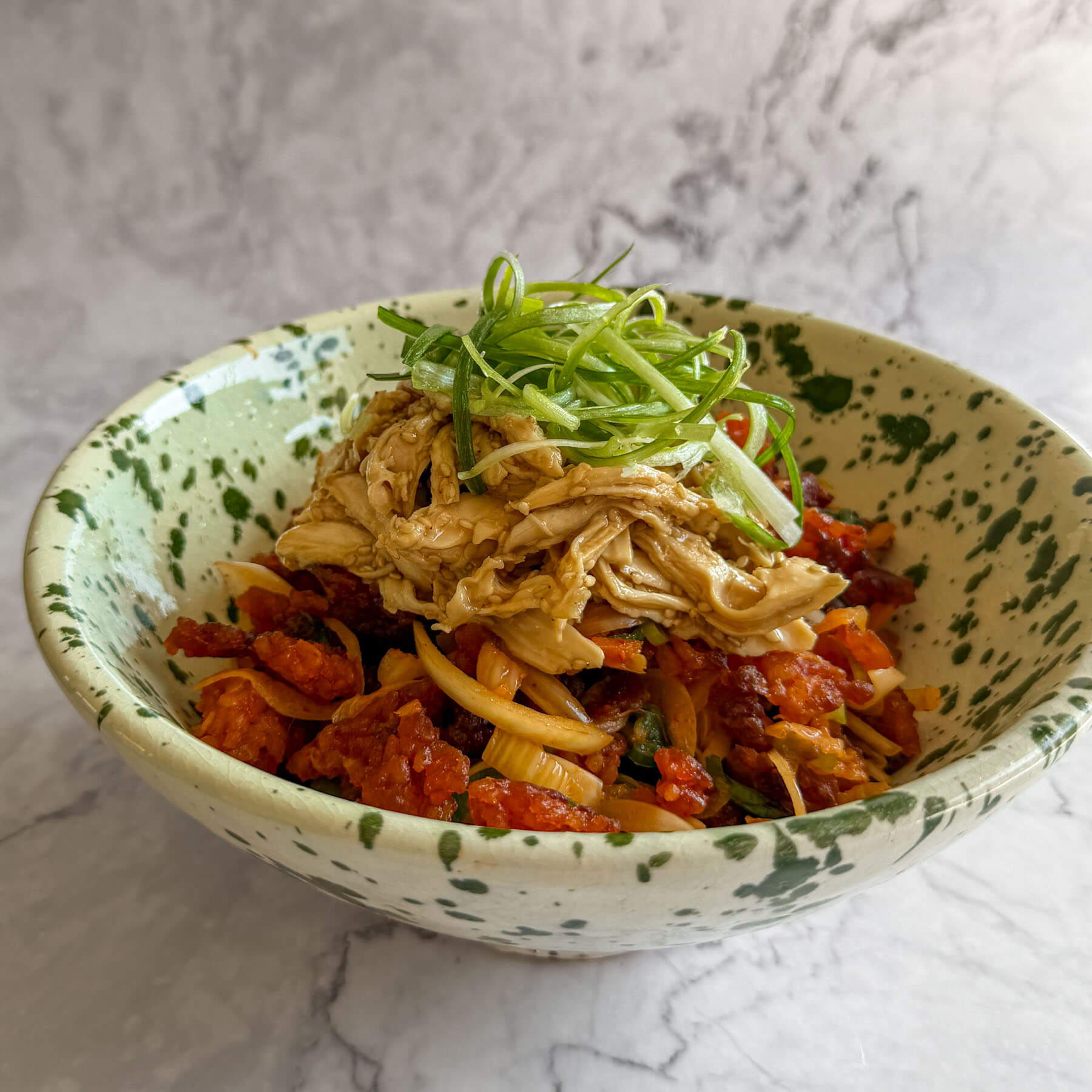 Gochujang crispy rice, topped with pulled sesame chicken and sliced spring onions.