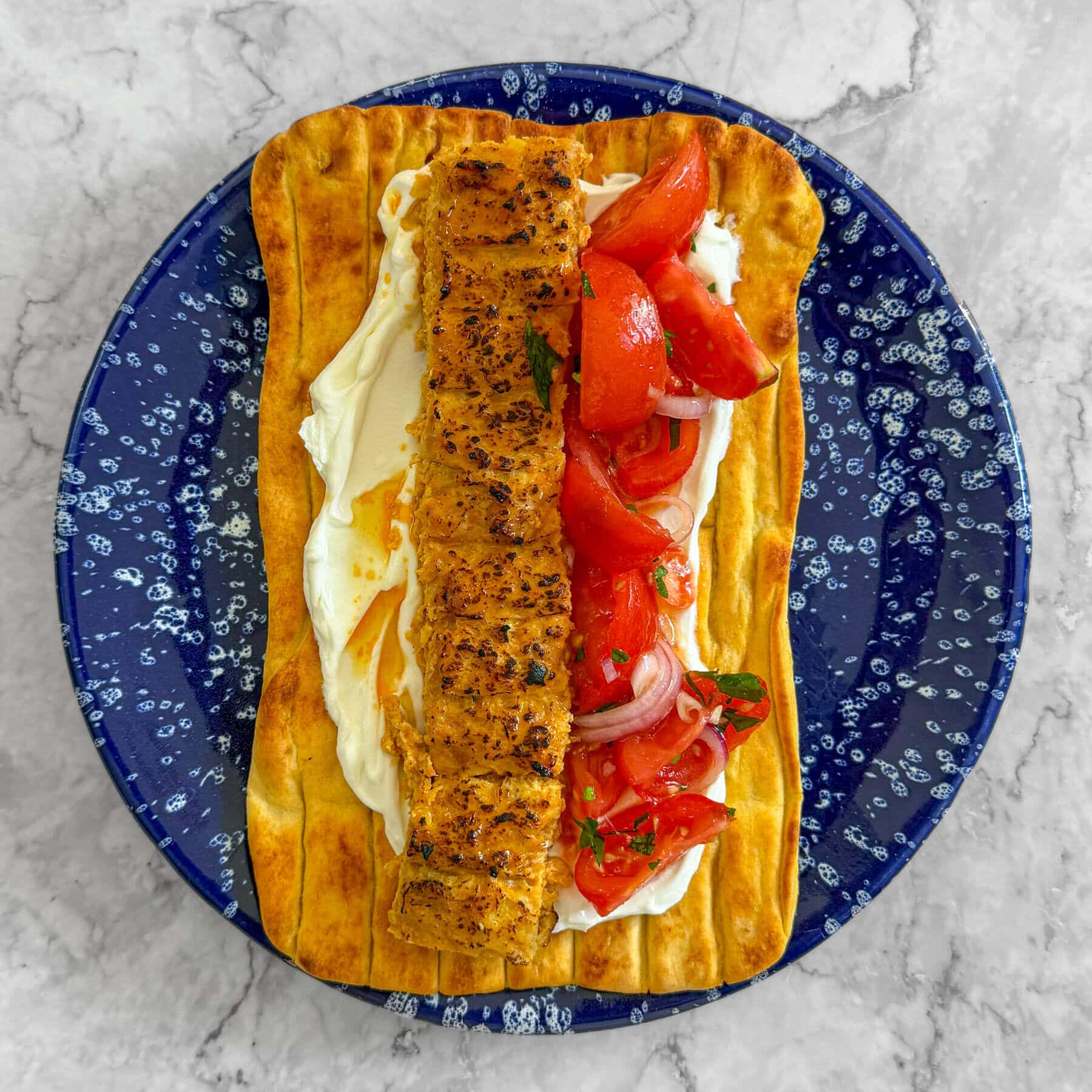 Saffron sheet pan chicken kebab, served on a flatbread with yoghurt and a tomato and herb salad.