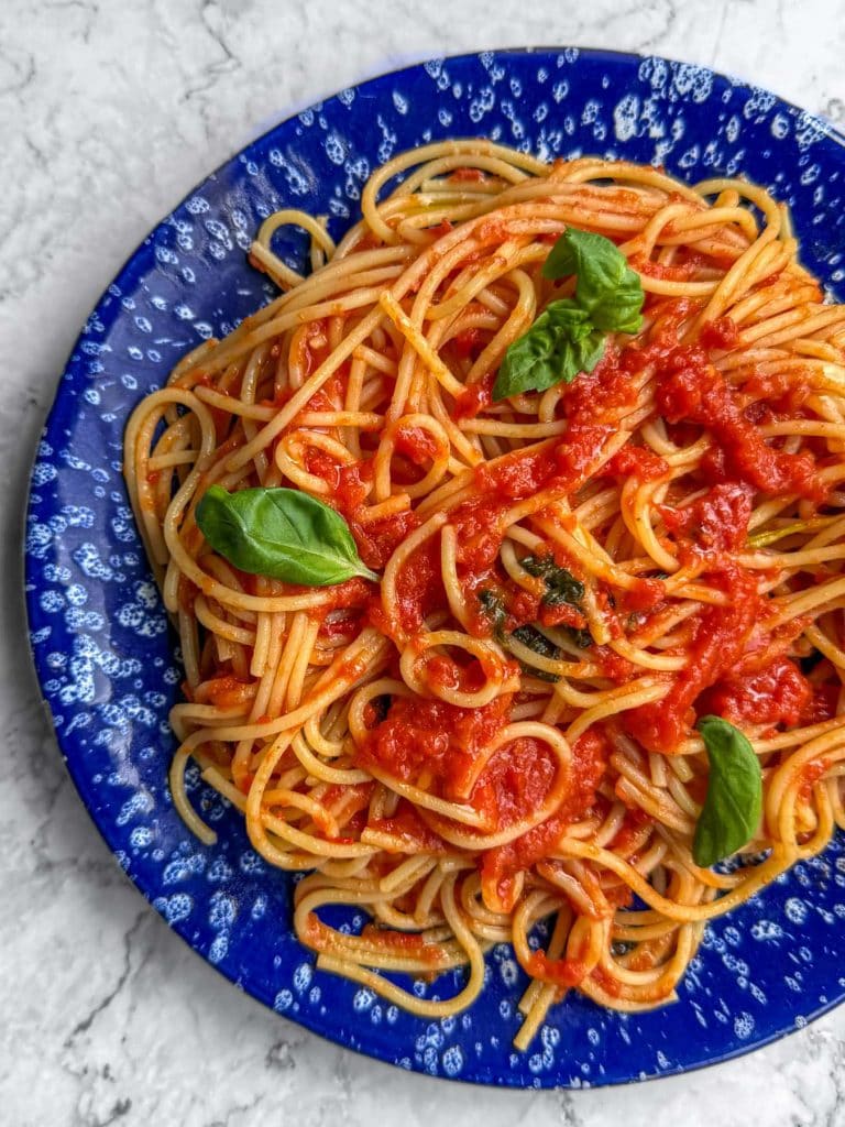 A closeup of brown butter tomato pasta, served on a blue speckled plate, topped with fresh basil leaves.