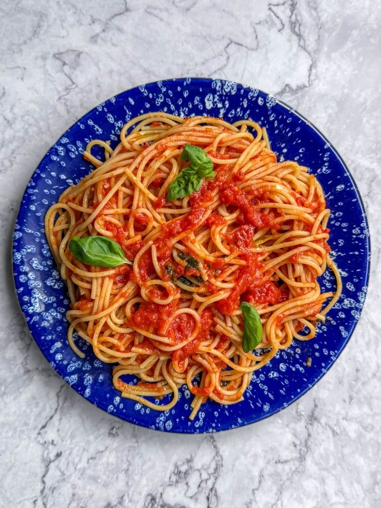 Brown butter tomato pasta, served on a blue speckled plate, topped with fresh basil leaves.