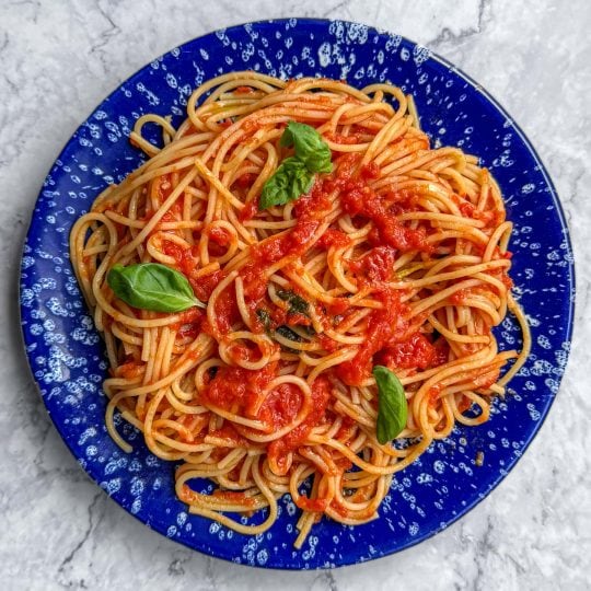 Brown butter tomato pasta, served on a blue speckled plate.