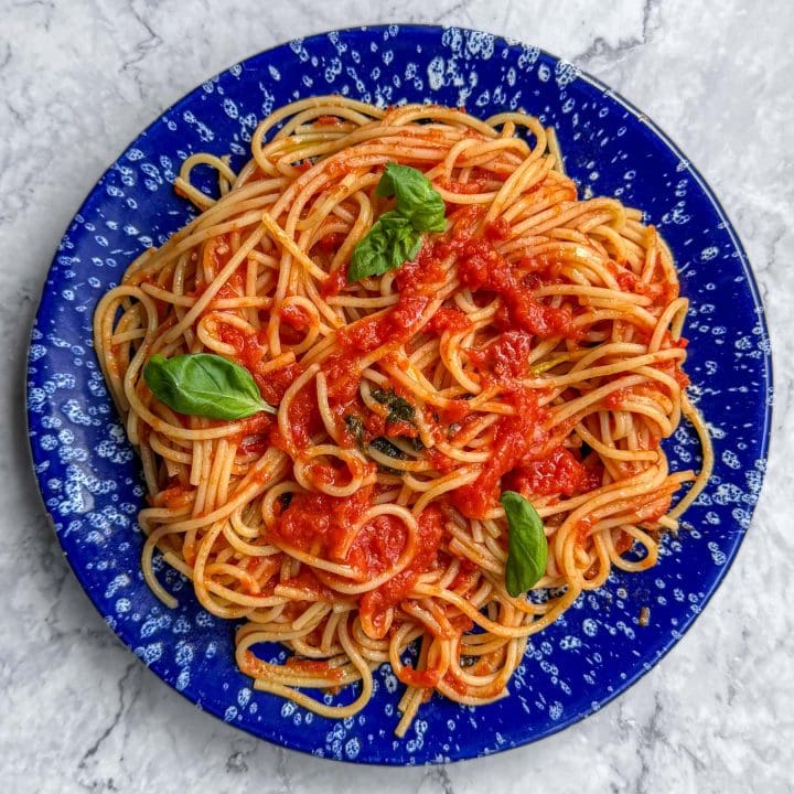 Brown butter tomato pasta, served on a blue speckled plate.