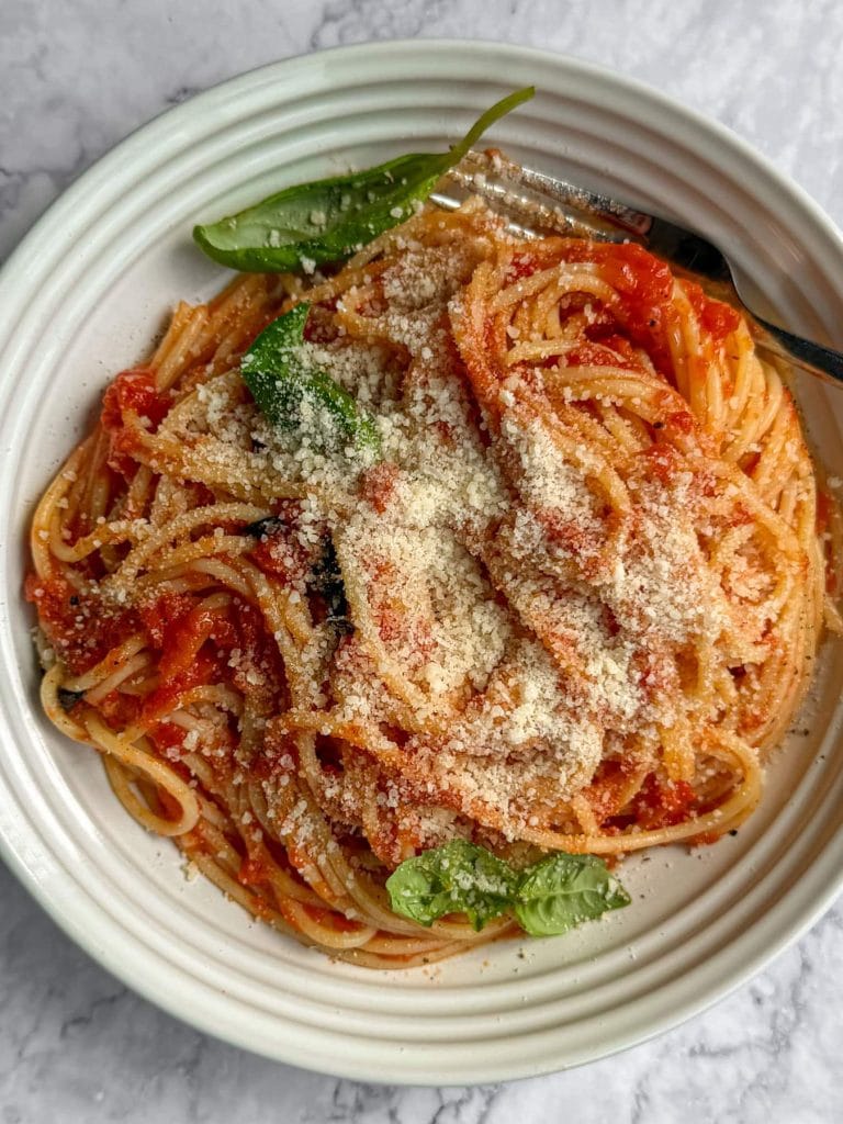Spaghetti tossed in a tomato and brown butter sauce, serve in a white shallow bowl and topped with parmesan and basil.
