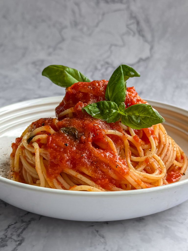 Spaghetti tossed in a tomato and brown butter sauce, serve in a white shallow bowl.