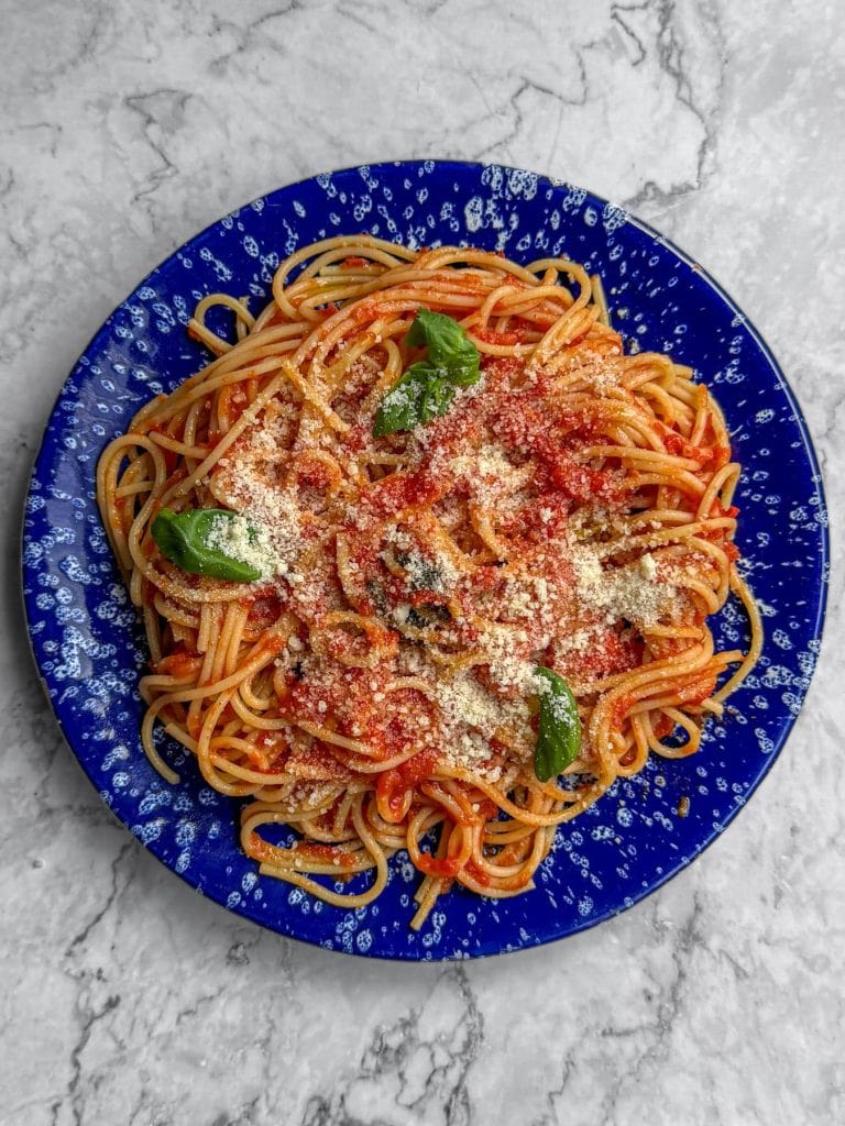Brown butter tomato pasta, served on a blue speckled plate, topped with grated parmesan.