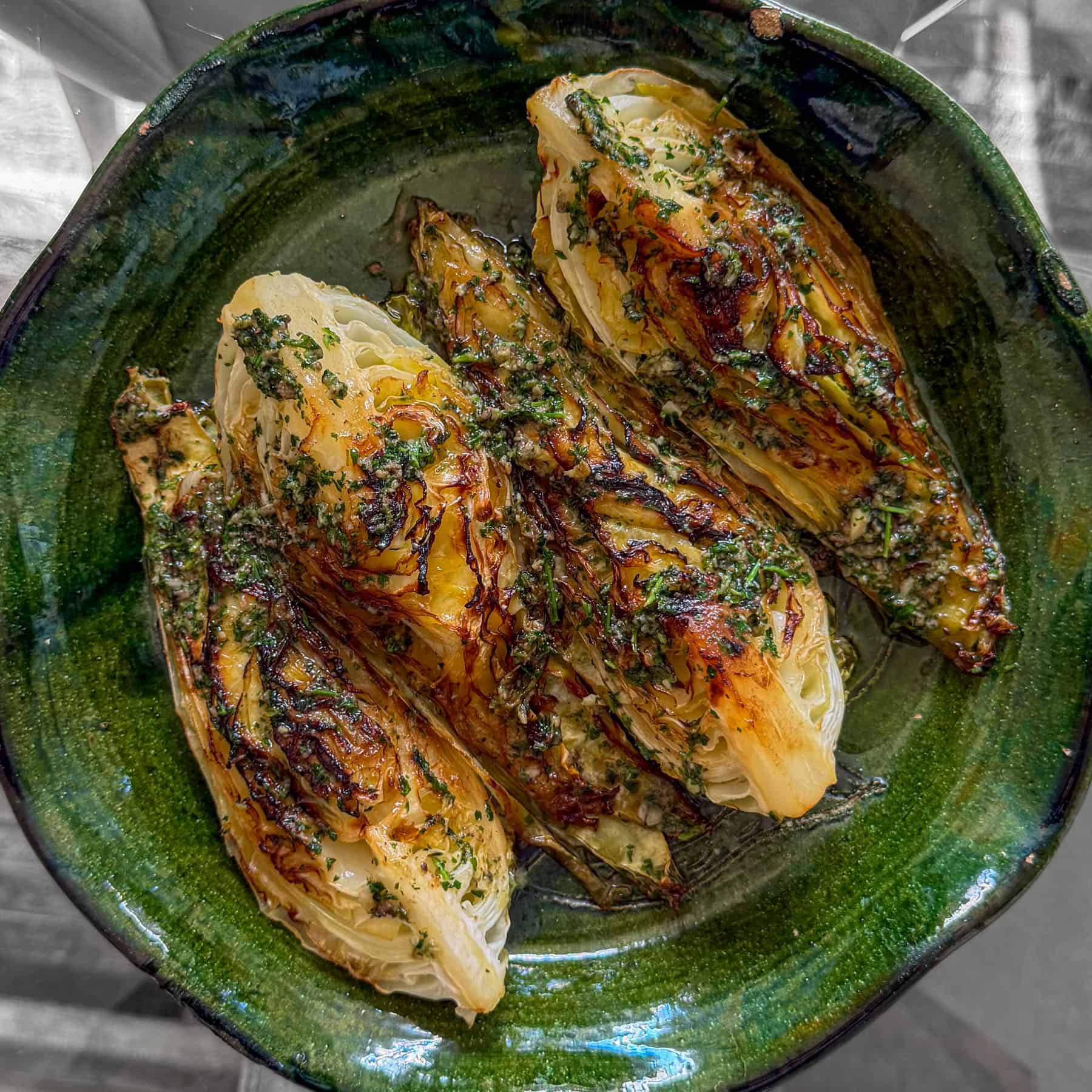 Charred hispi cabbage, based in anchovy garlic butter and served on a green plate.
