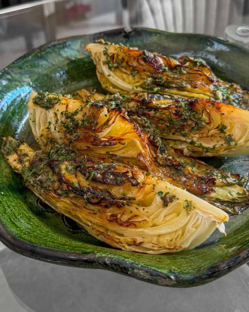 A side-on shot of charred hispi cabbage, topped with anchovy butter and served on a green platter.