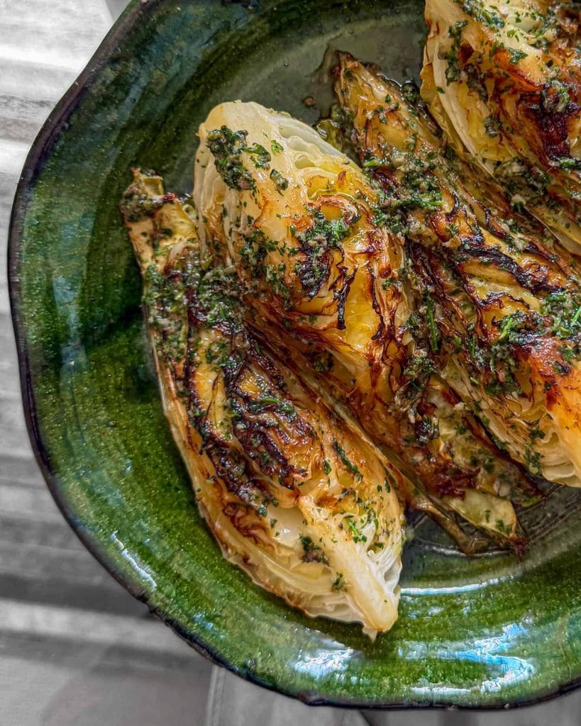 A close-up shot of charred hispi cabbage, topped with anchovy butter and served on a green platter.