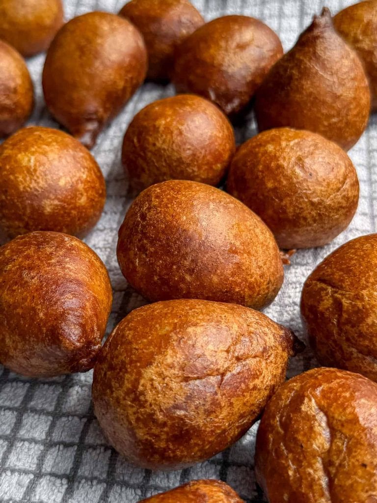A closeup of freshly fried plantain puff puff draining on a tea towel