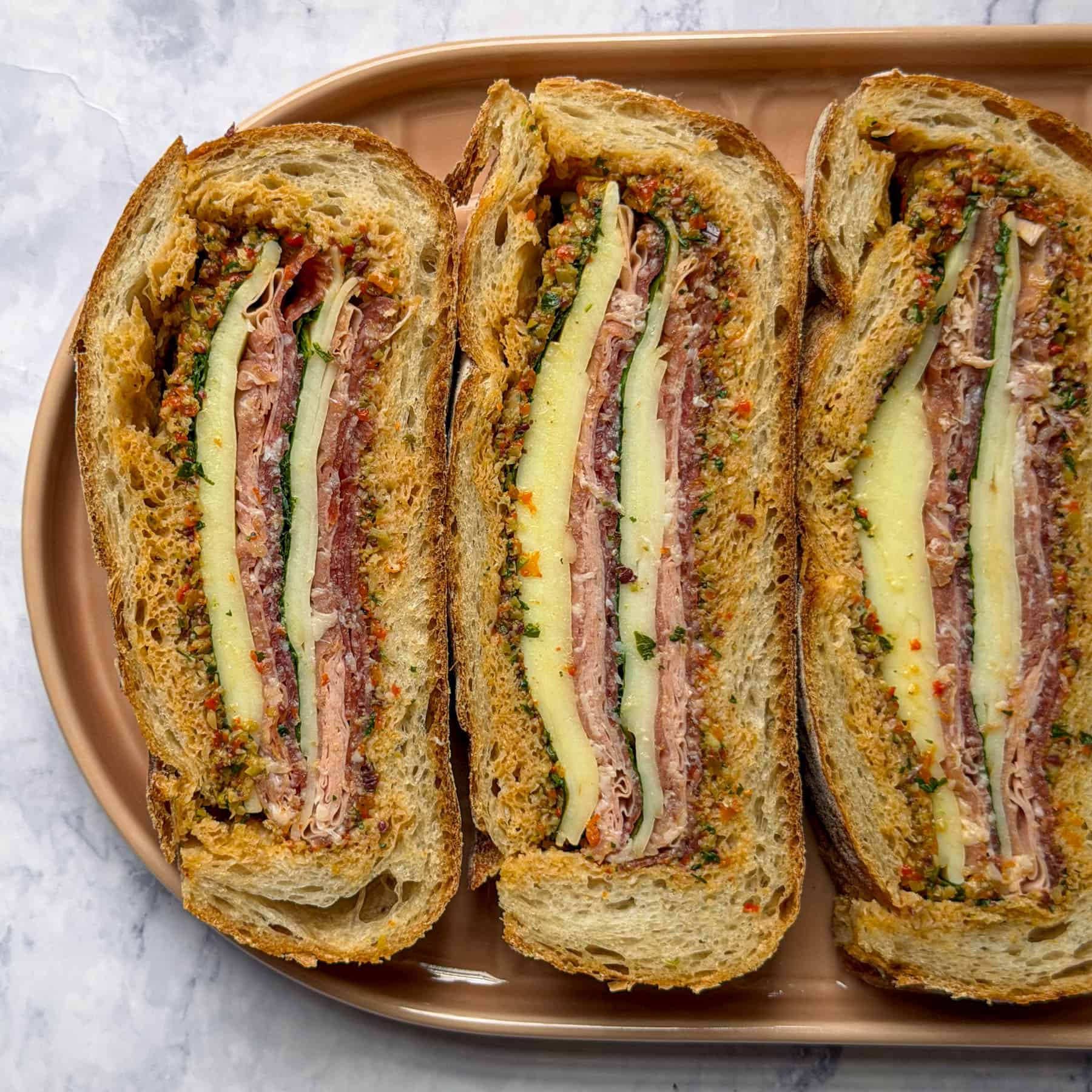 Muffuletta sandwich filled with homemade olive salad, Italian cured meats and cheese.