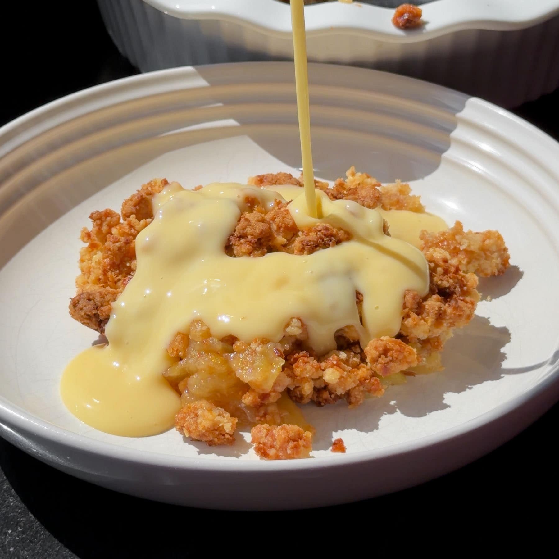 Pouring custard over the almond croissant apple crumble.