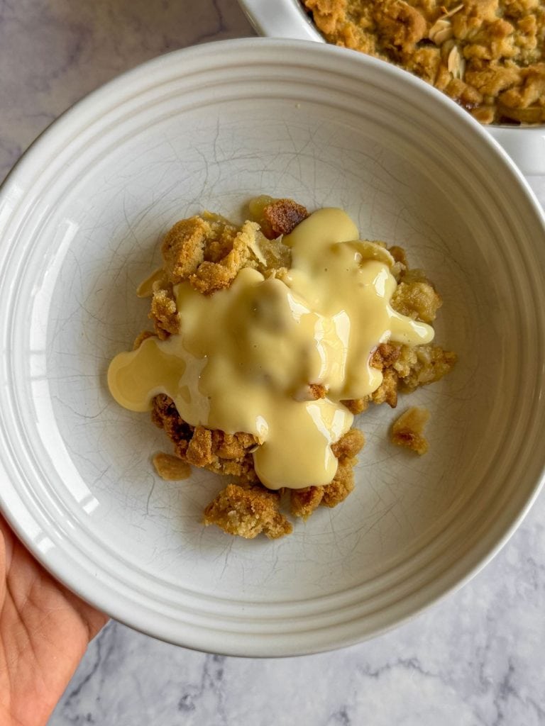 Overhead shot of almond croissant apple crumble, topped with custard.