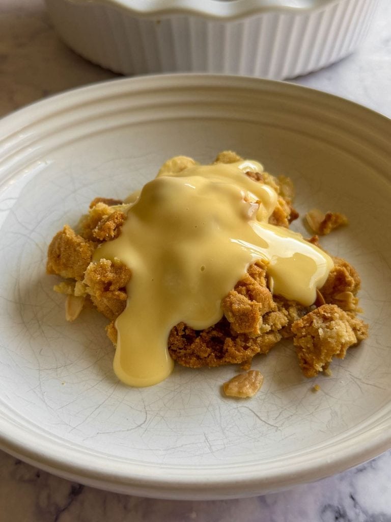 A side-on shot of almond croissant apple crumble, topped with custard.