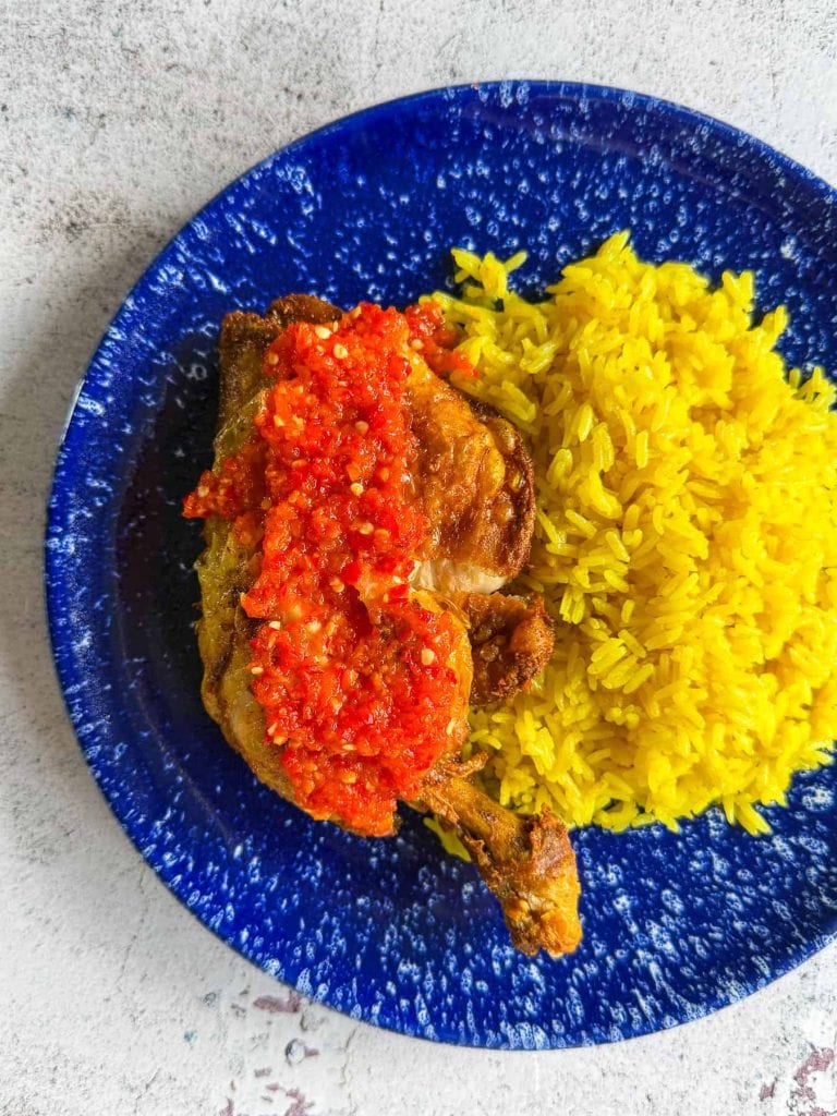 A closeup of Indonesian smashed fried chicken with sambal and golden rice