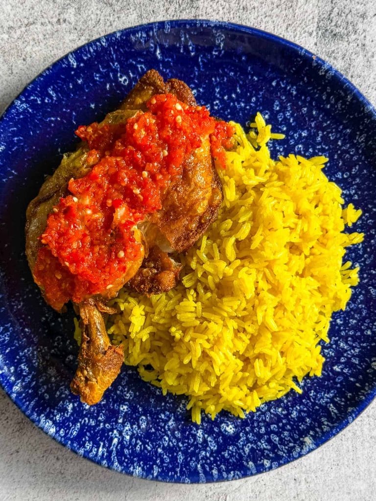 A close up shot of ayam penyet Indonesian fried chicken served with spicy sambal and golden jasmine rice
