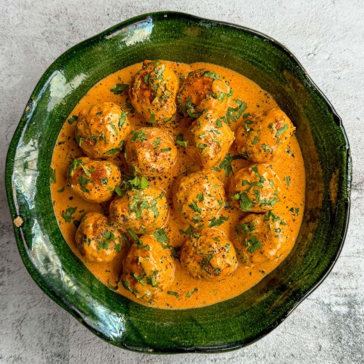 Coconut harissa chicken meatballs, served in a green shallow bowl.