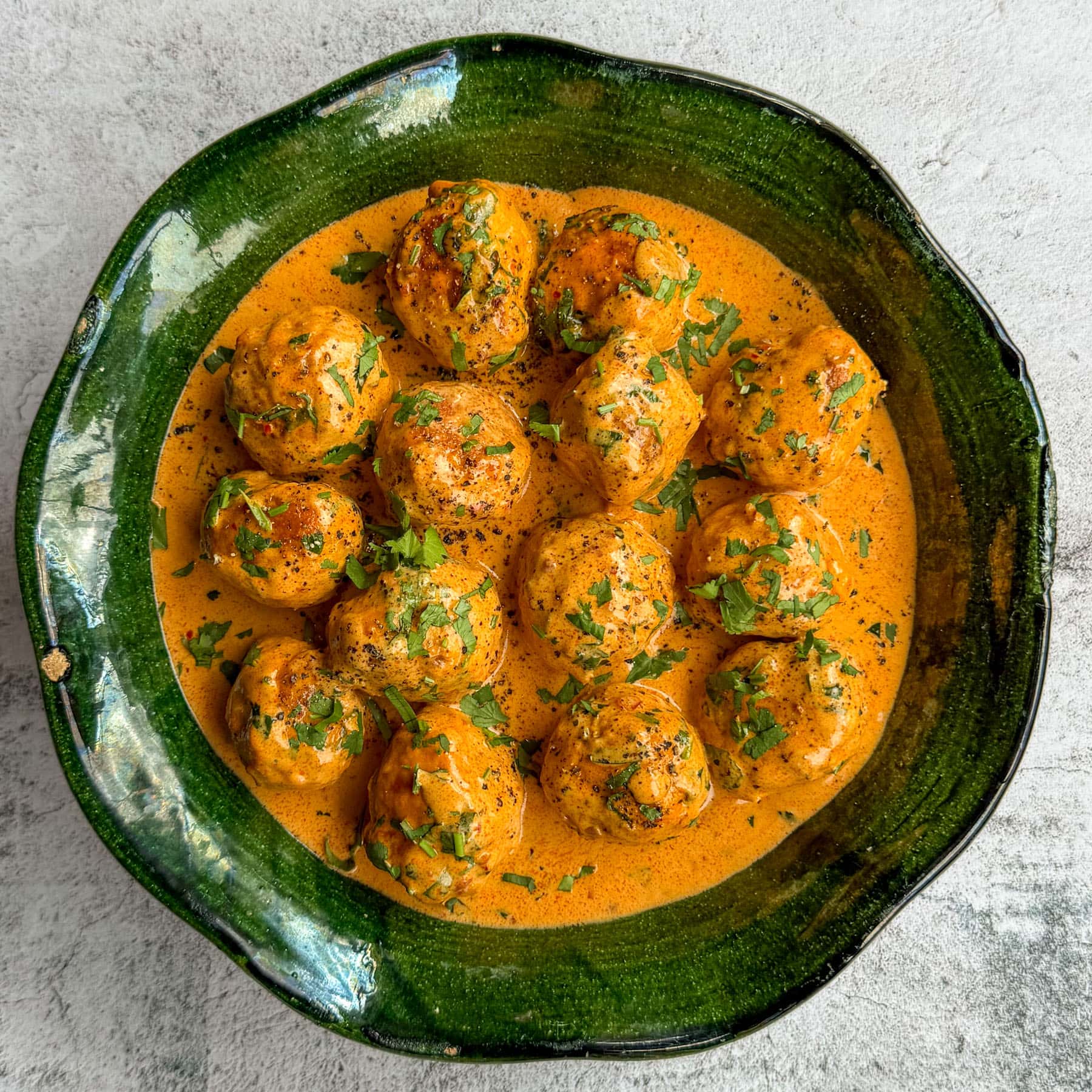 Coconut harissa chicken meatballs, served in a green shallow bowl.