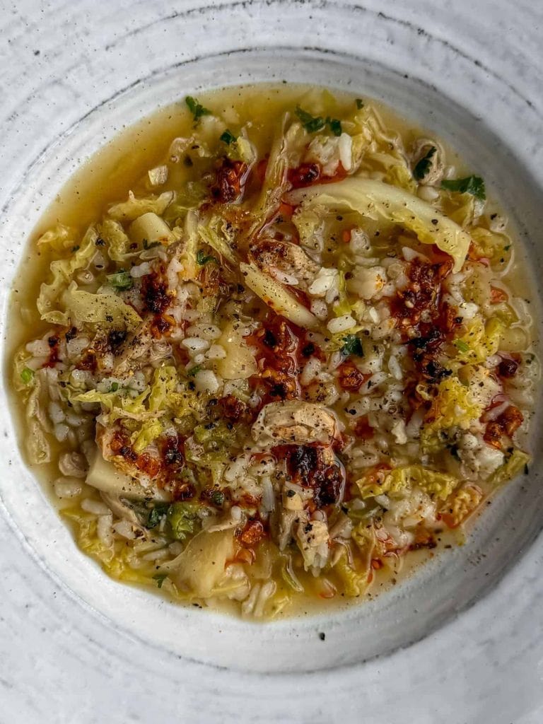 A bowl of ginger and lemongrass chicken cabbage soup, topped with chilli oil.