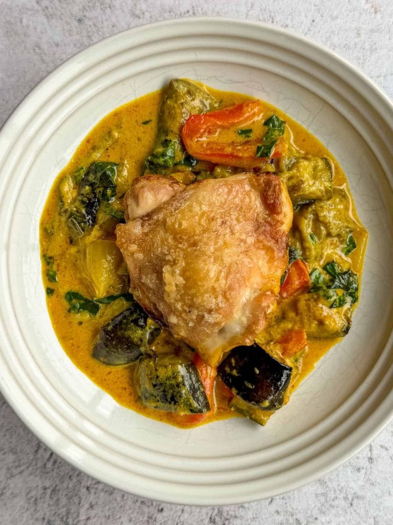 An individual portion of Thai curry chicken traybake with golden chicken thighs, roasted vegetables and coconut curry sauce